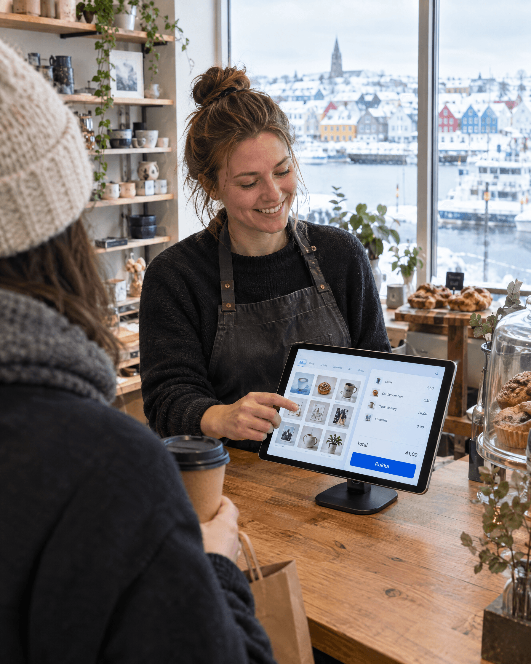 Í lítilli verslun og kaffihúsi stimplar afgreiðslukona söluna inn í afgreiðslukerfið á spjaldtölvu við kassann.